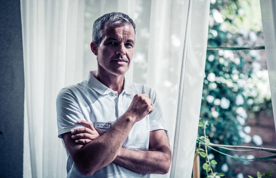 Mitarbeiter im Wellnesshotel Preidlhof Ein Mitarbeiter im weißen Poloshirt steht vor einem Fenster mit Gardinen und blickt in die Kamera.