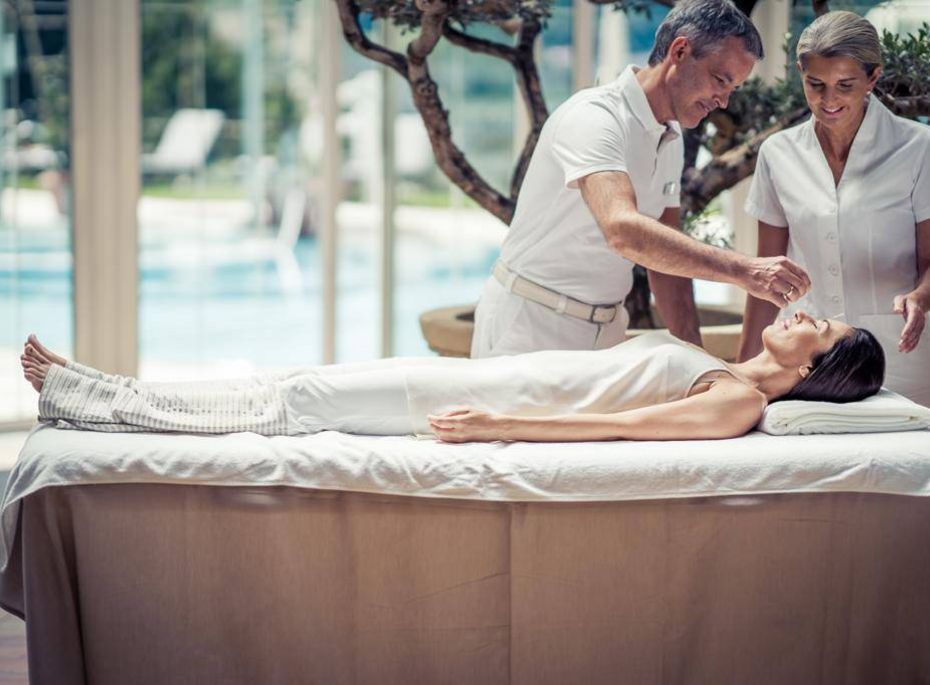 Massage im Wellnesshotel in Naturns Ein Mann und eine Frau behandeln eine liegende Frau auf einer Liege im Spa-Bereich.