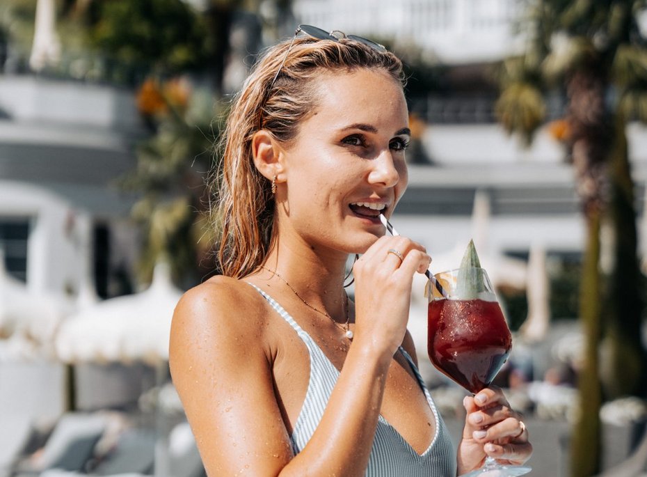 Eine Frau, im Badeanzug, mit einem Cocktail in der Hand.