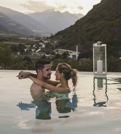 Frau umarmt Mann im Pool mit Landschaftskulisse im Hintergrund